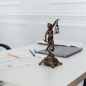 pexels-photo-7876093-7876093 A legal professional's workspace featuring Lady Justice statue, documents, and a laptop.